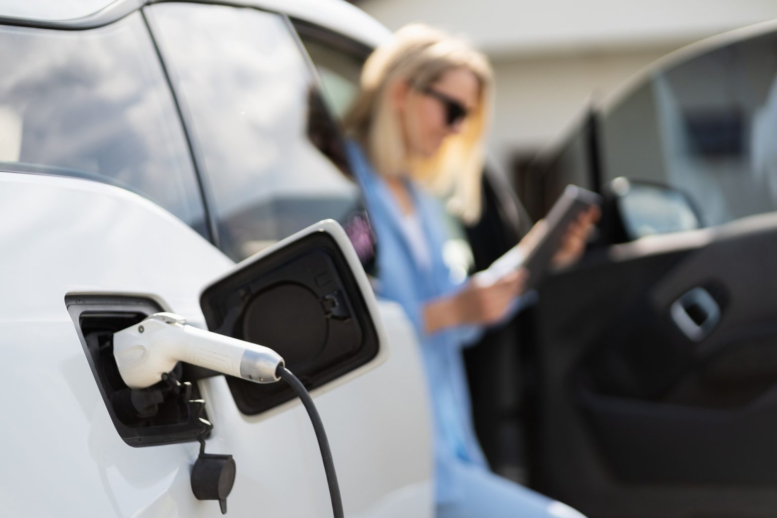 Woman Charging Electric Car and Using Smartphone Outdoors